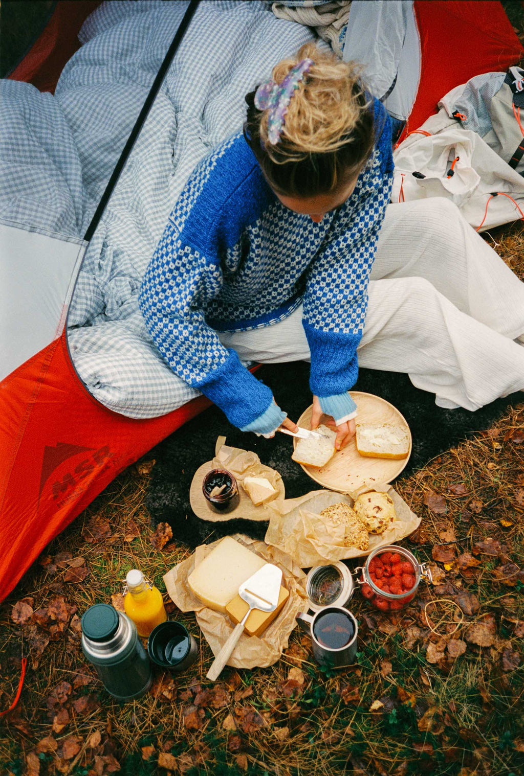 Person preparing a picnic inside a tent with food and drinks on the ground.