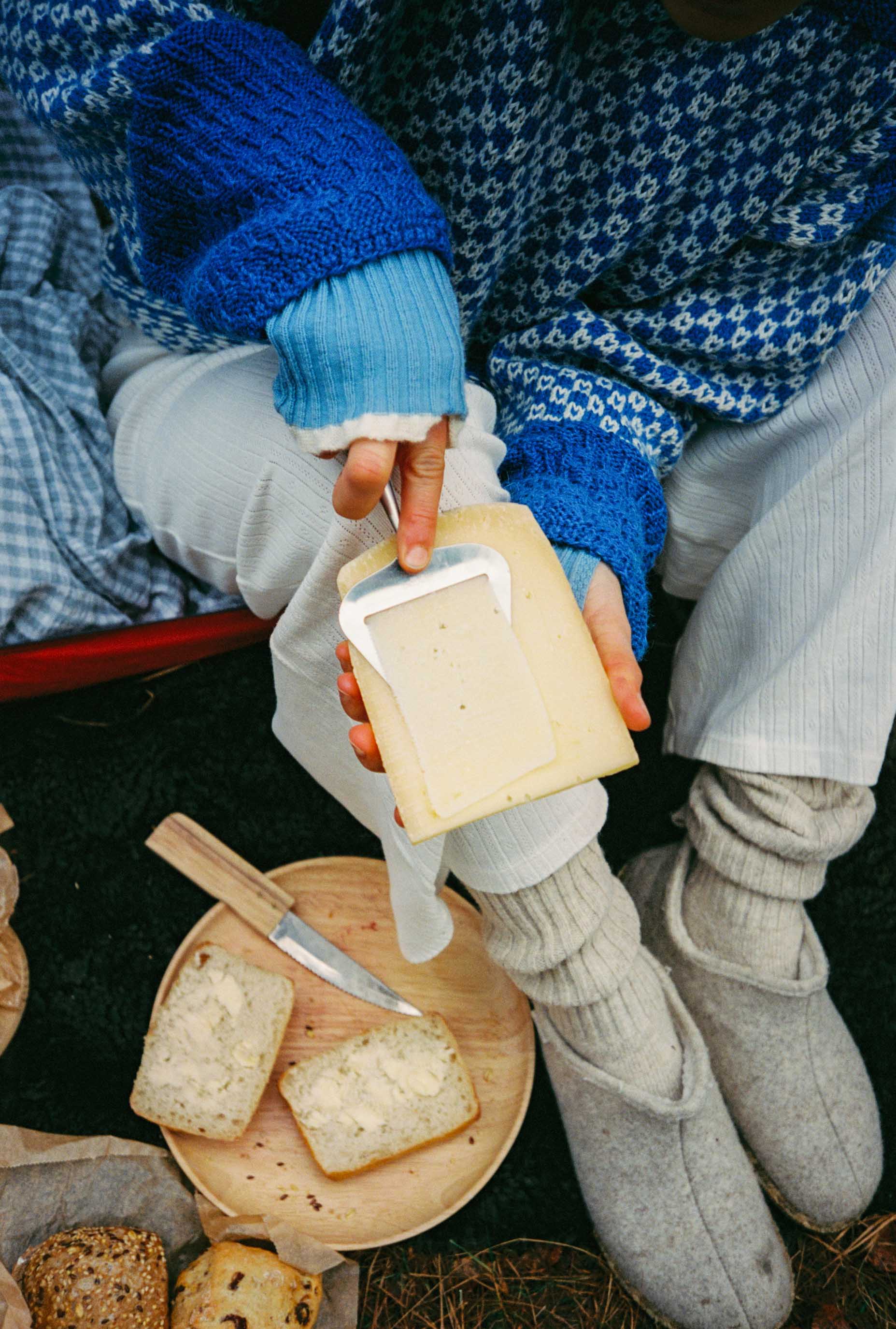 Person taking a slice of cheese, wearing a blue sweater and gray pants.